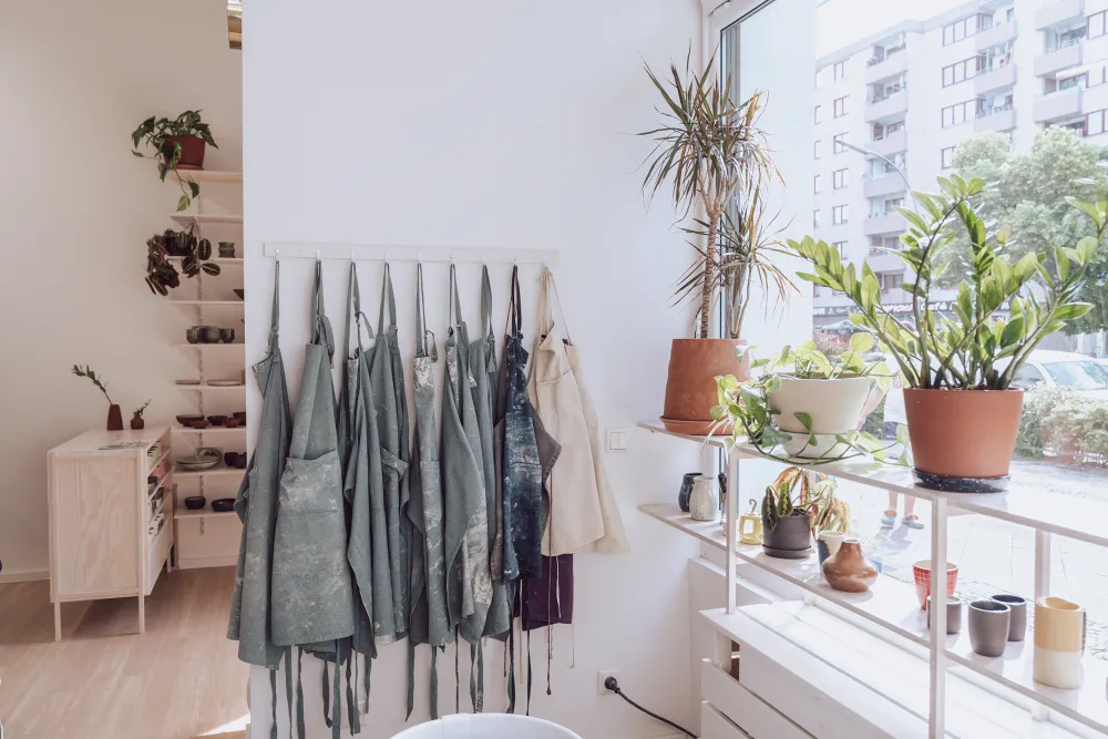 Keramikwerkstatt mit Schürzen, das Schaufenster ist im Anschnitt zu sehen, im Hintergrund sieht man das Verkaufsregal