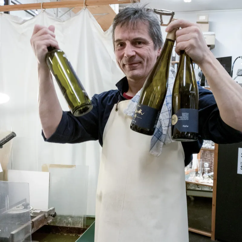 Mitarbeiter Christoph Hagedorn steht mit leeren Weinflaschen in der Hand an der Glassäge